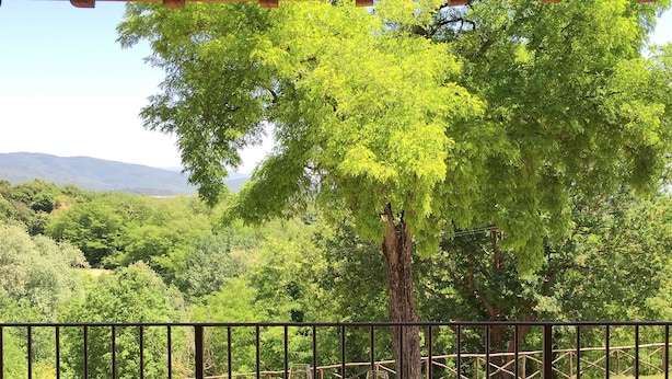 Una mesa de madera con dos sillas en un balcón, con vistas a un paisaje verde y exuberante con árboles y colinas.