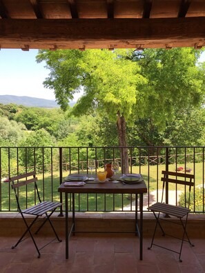 Una mesa de madera con dos sillas en un balcón, con vistas a un paisaje verde y exuberante con árboles y colinas.