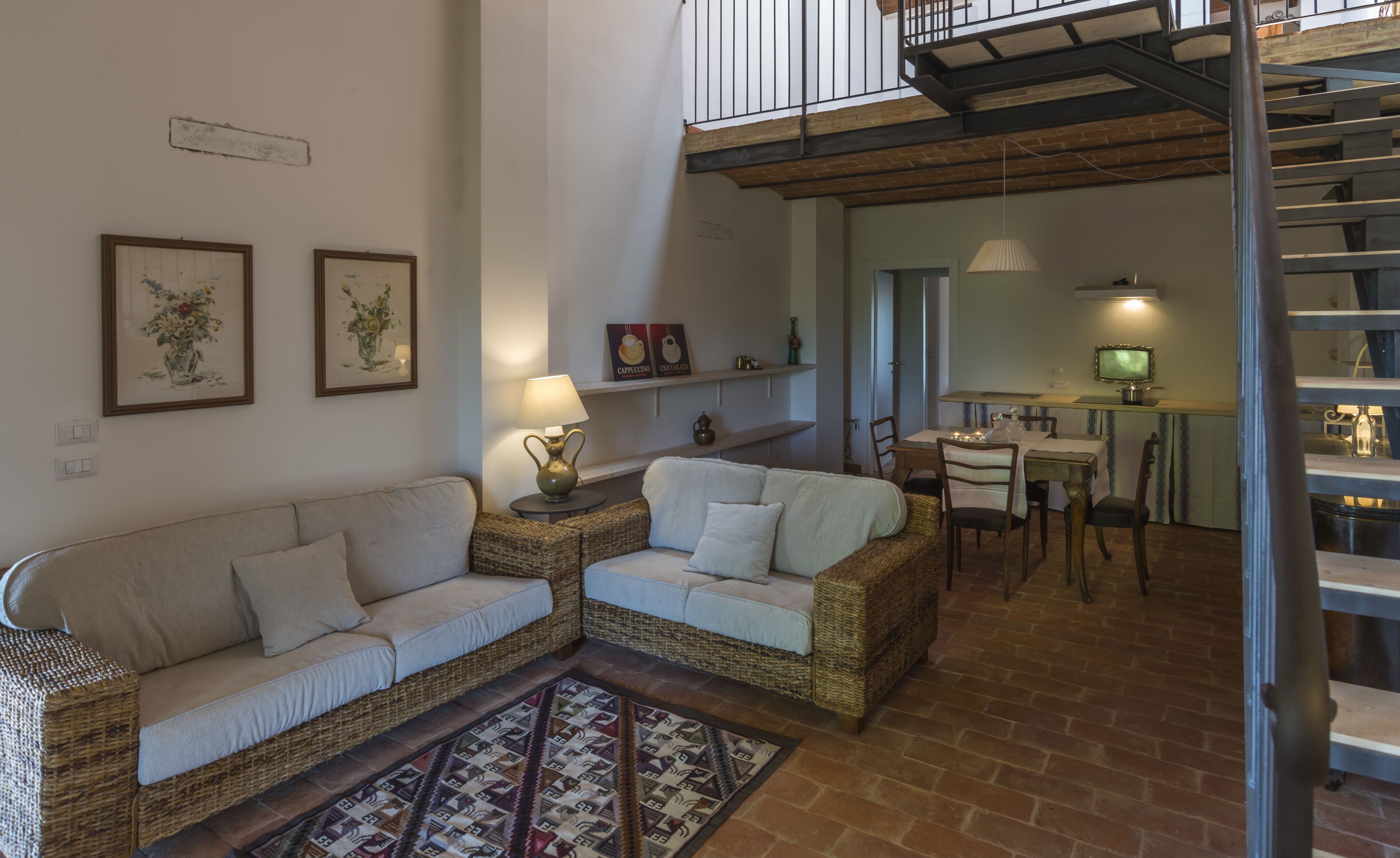 Een gezellige woonkamer met een bank en twee fauteuils, een eethoek met een tafel en stoelen, en een trap met een balkon.
