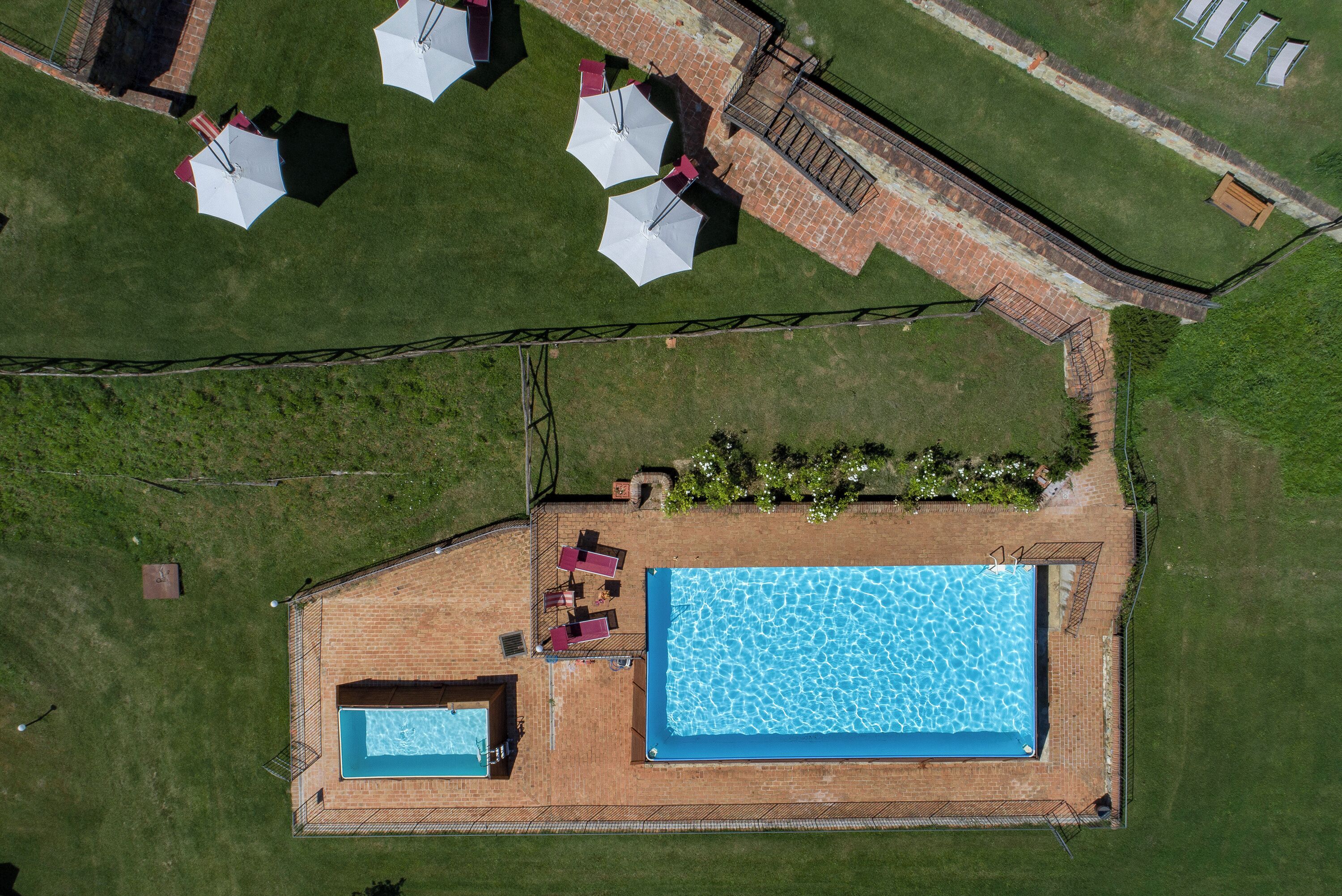 An aerial view of a property with a swimming pool, a patio area with umbrellas, and a brick structure.
