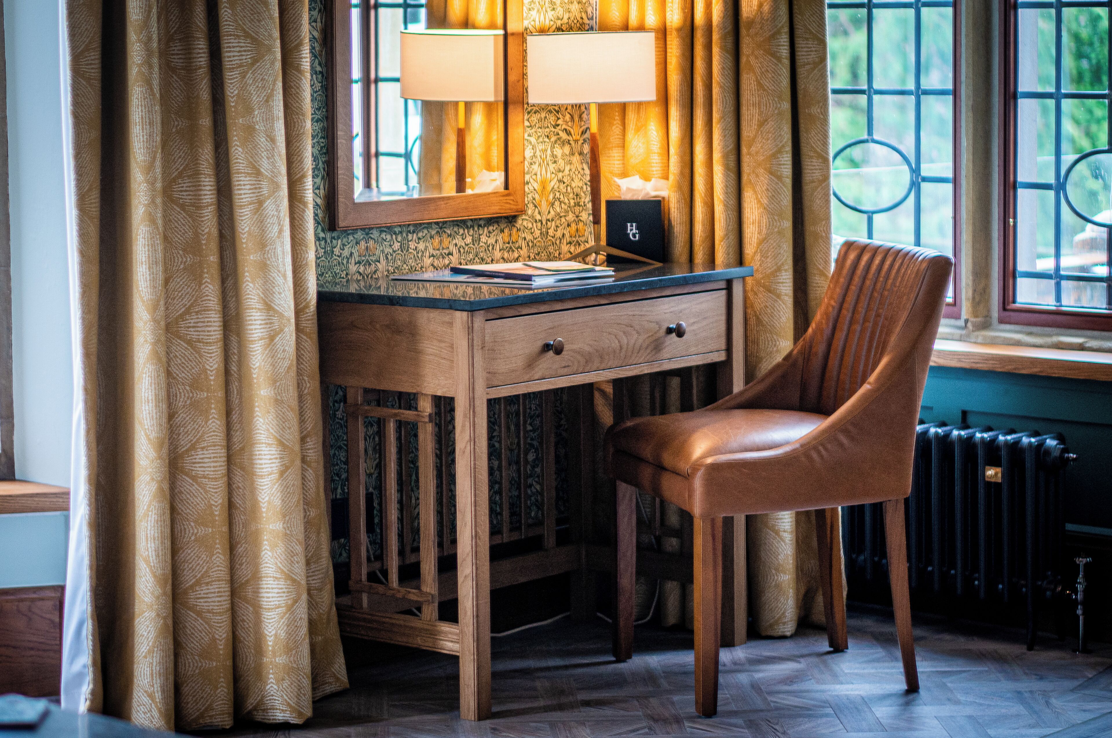 A wooden desk with a lamp, a chair, and a window with a view.