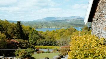 A view from a balcony overlooking a lake with mountains in the distance, surrounded by lush greenery and a stone building.