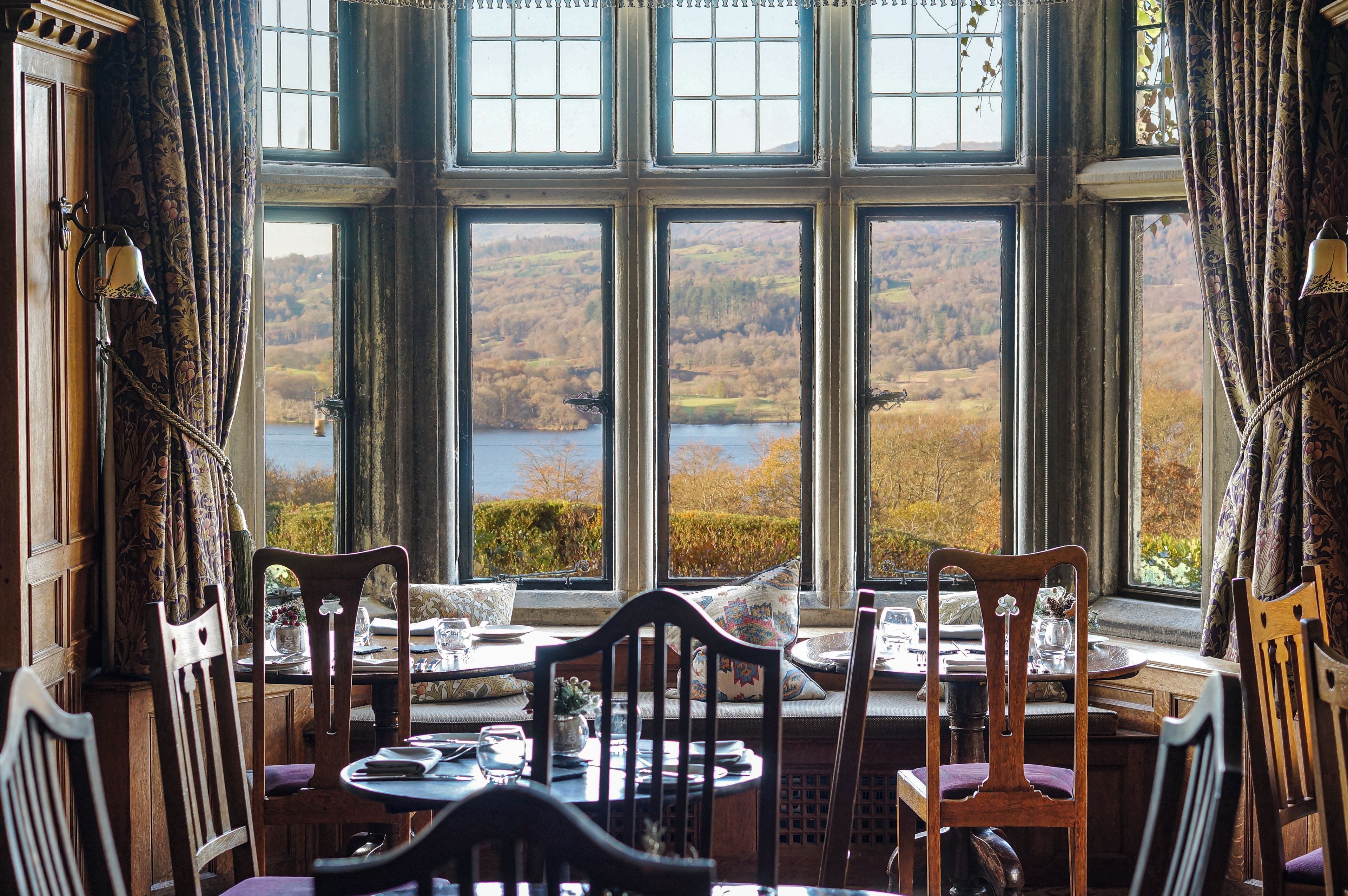 Un comedor con una mesa dispuesta para dos personas, con vistas a un paisaje pintoresco de un lago y colinas.