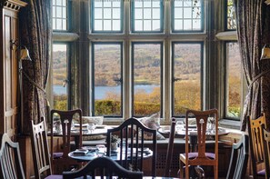 A dining area with a table set for two, overlooking a scenic view of a lake and hills. - Holbeck Ghyll Country House Estate (Windermere)