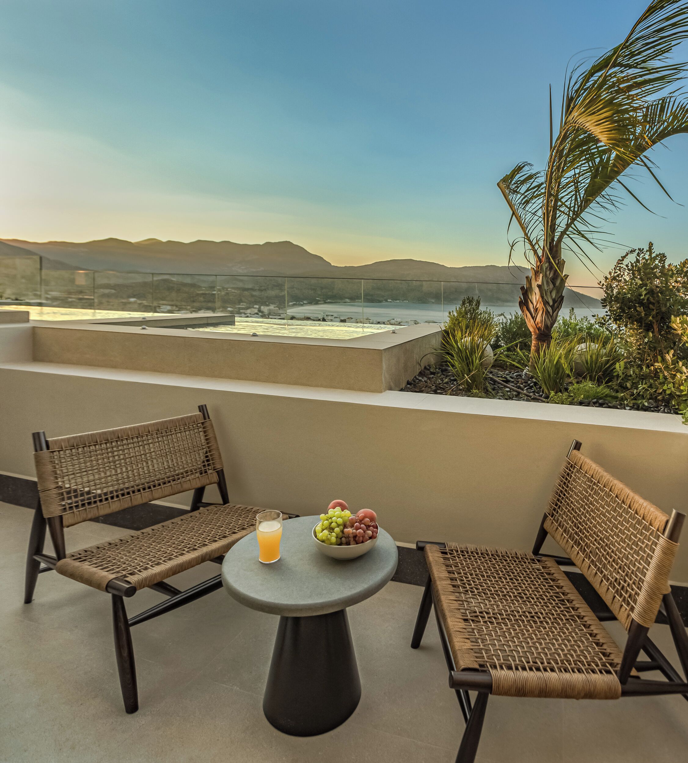 A terrace with two wicker chairs, a small round table, a bowl of fruit, and a glass of orange juice.