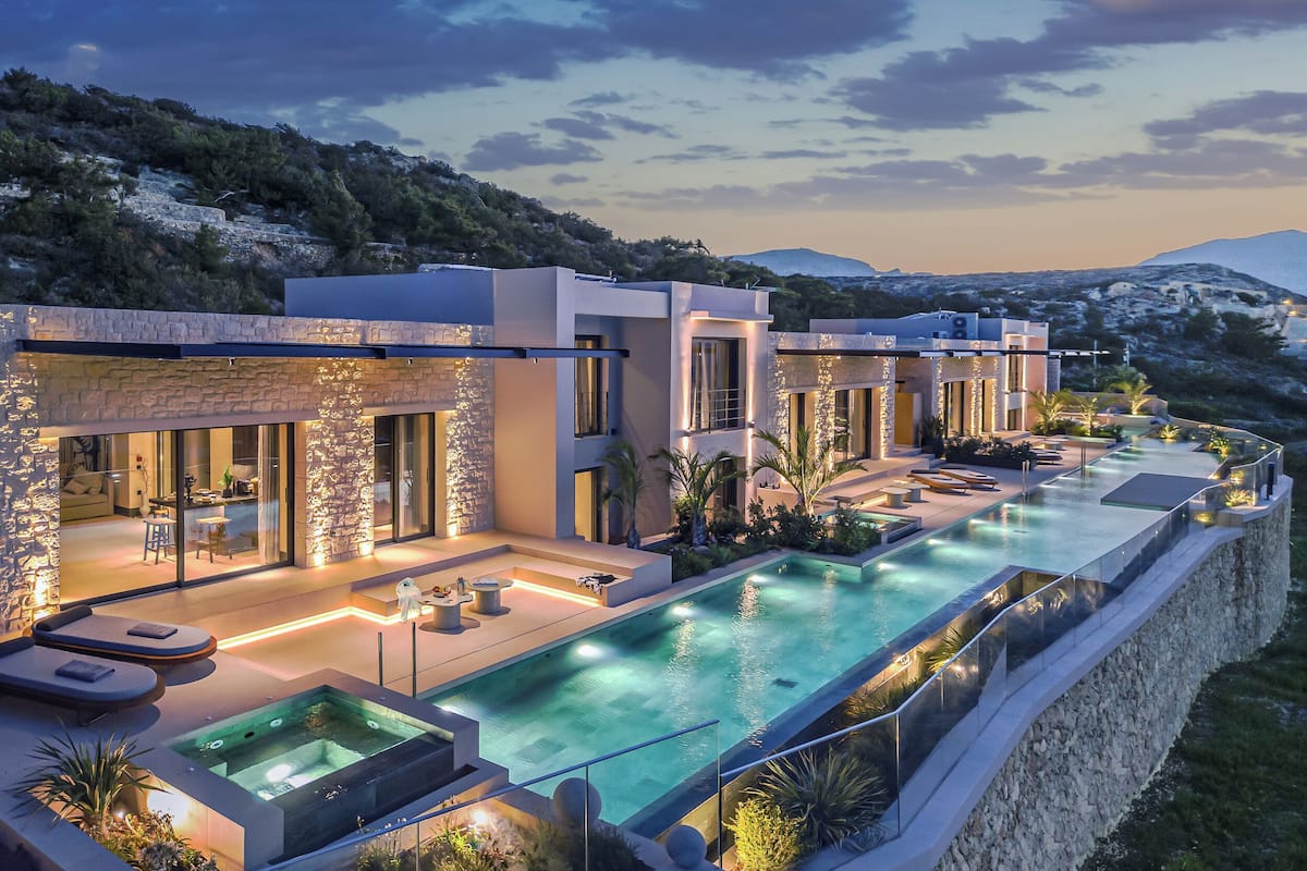 A modern resort with a large infinity pool, outdoor seating, and a view of the surrounding landscape.
