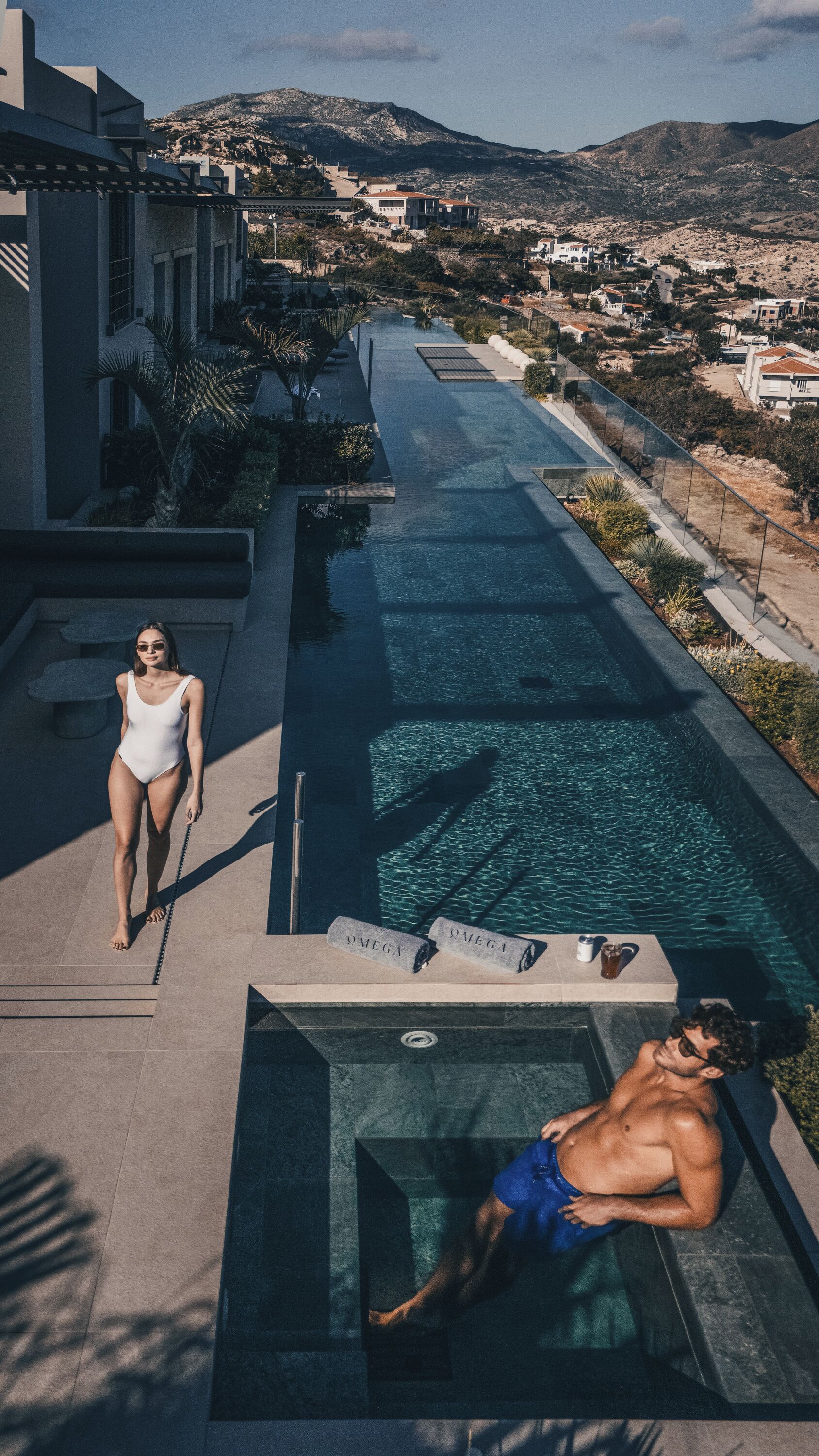 A pool area with a clear view of the surrounding landscape, including mountains and a distant village.