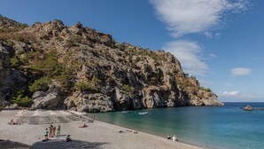 Een rotsachtige kustlijn met helder turquoise water, parasols en mensen die ontspannen.