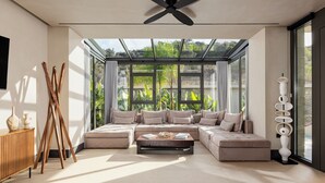 Een moderne woonkamer met een modulaire bank, een plafondventilator en grote ramen met uitzicht op groen.