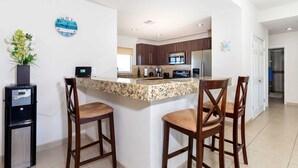 Una cocina moderna con una isla central, taburetes de bar, una cafetera y un reloj decorativo.
