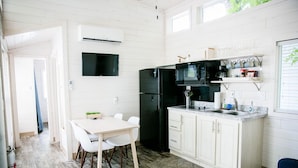 A compact kitchen with white cabinetry, a black refrigerator, a microwave, and a coffee machine. There is a small dining area with a white table and chairs. - Lakefront Two Bedroom Cabin #37 (Charlotte)