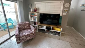 En stue med fjernsyn, en stribet sofa, en reol og en skydedør, der fører til et udendørs område.
