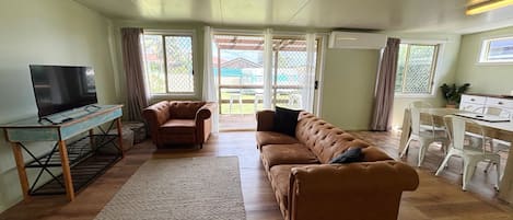 Una sala de estar con sofá, televisión, mesa de comedor con sillas y zona de cocina.