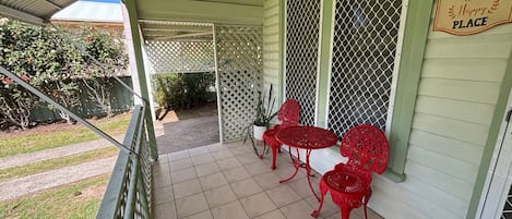 A covered porch with a 'Welcome to Our Happy Place' sign, red metal chairs, and a potted plant.