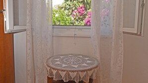 A room with a wooden floor, a small round table with a lace tablecloth, a bench, and a window with white curtains. - House VERONIKA,sea views, charming terrace,tranquility and natural beauty. (Drvenik Veliki)