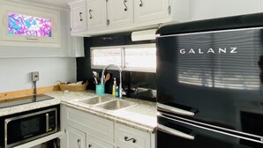 A compact kitchen with white cabinets, a black Galanz refrigerator, a microwave, and a window with a view. - Unique Lakefront House Boat at Long Cove Resort (Charlotte)
