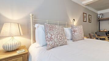 A neatly made bed with floral-patterned pillows, a bedside lamp, and a chair in a well-lit room with a simple, clean design.
