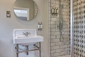 A bathroom with a white sink, a round mirror, a shower with a handheld showerhead, and tiled walls.