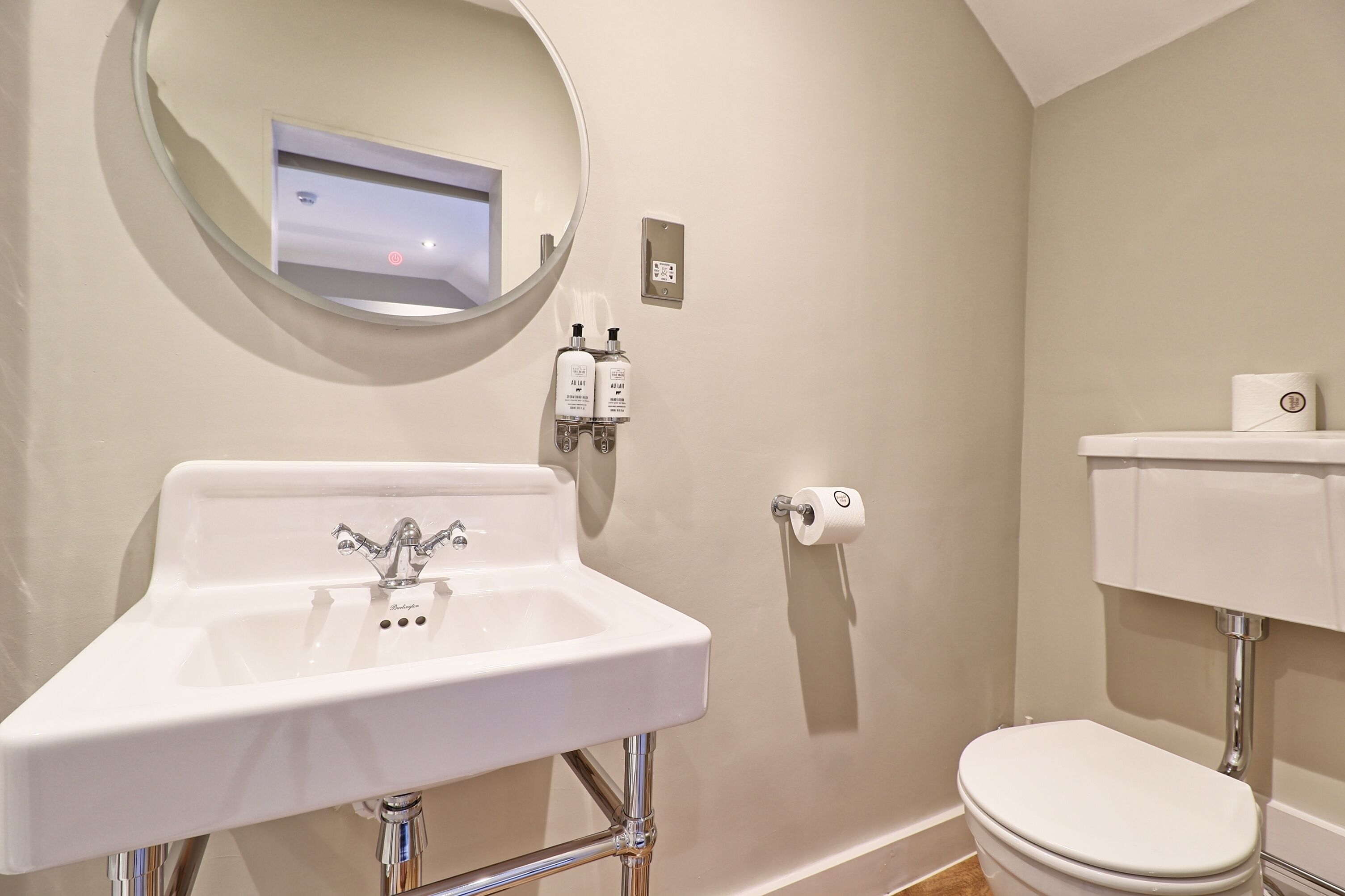 A bathroom with a white sink, a mirror, a toilet, and a wall-mounted soap dispenser.