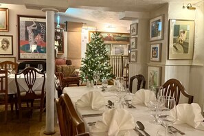 A dining area with a Christmas tree, framed pictures on the walls, and a table set for a meal. - Noble Goose Rooms (Colchester)
