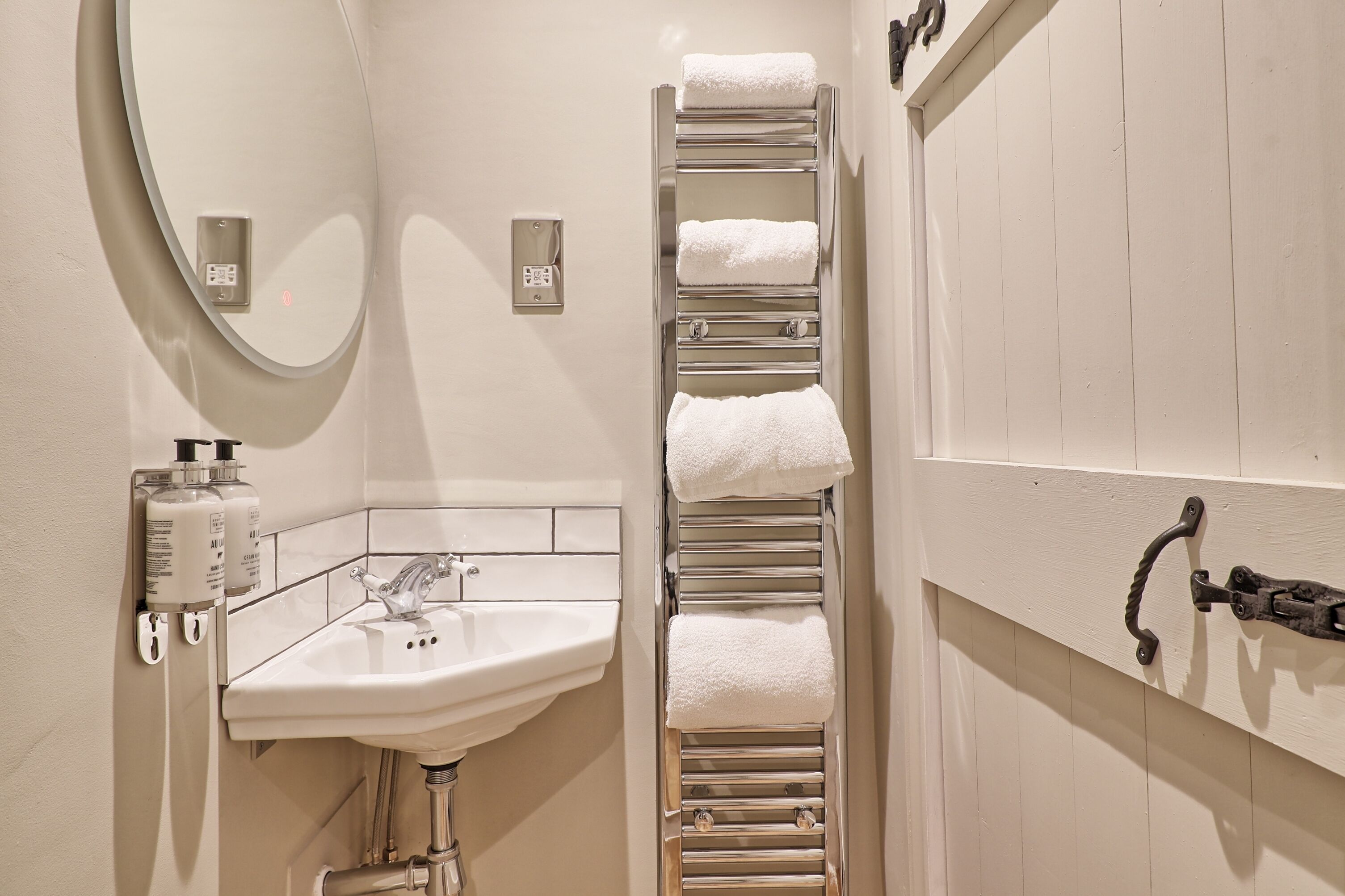Une salle de bain équipée d’un lavabo, d’un miroir, d’un porte-serviettes et d’un interrupteur fixé au mur.