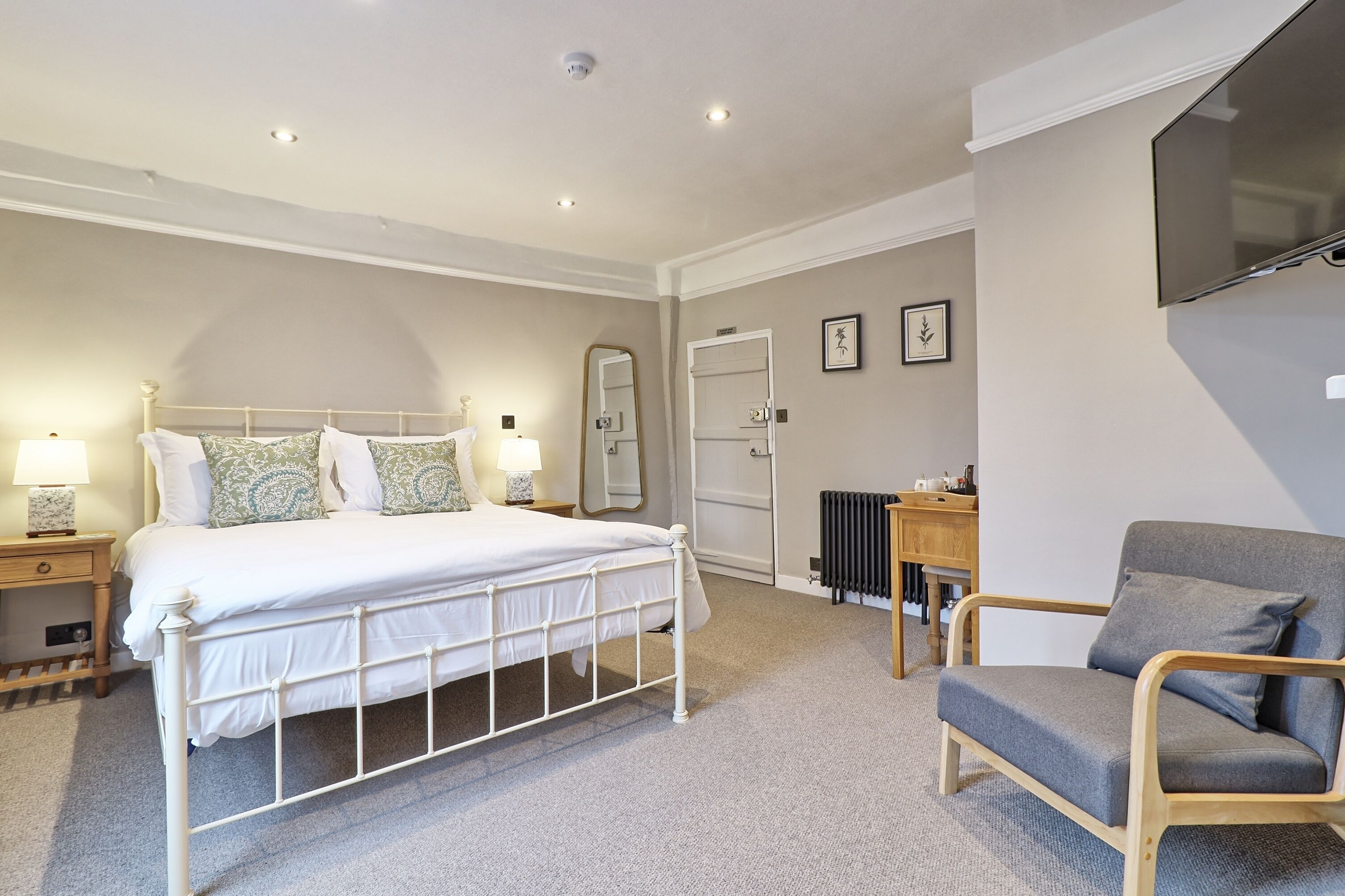 A bedroom with a bed, bedside tables, a chair, a mirror, a radiator, and a TV.