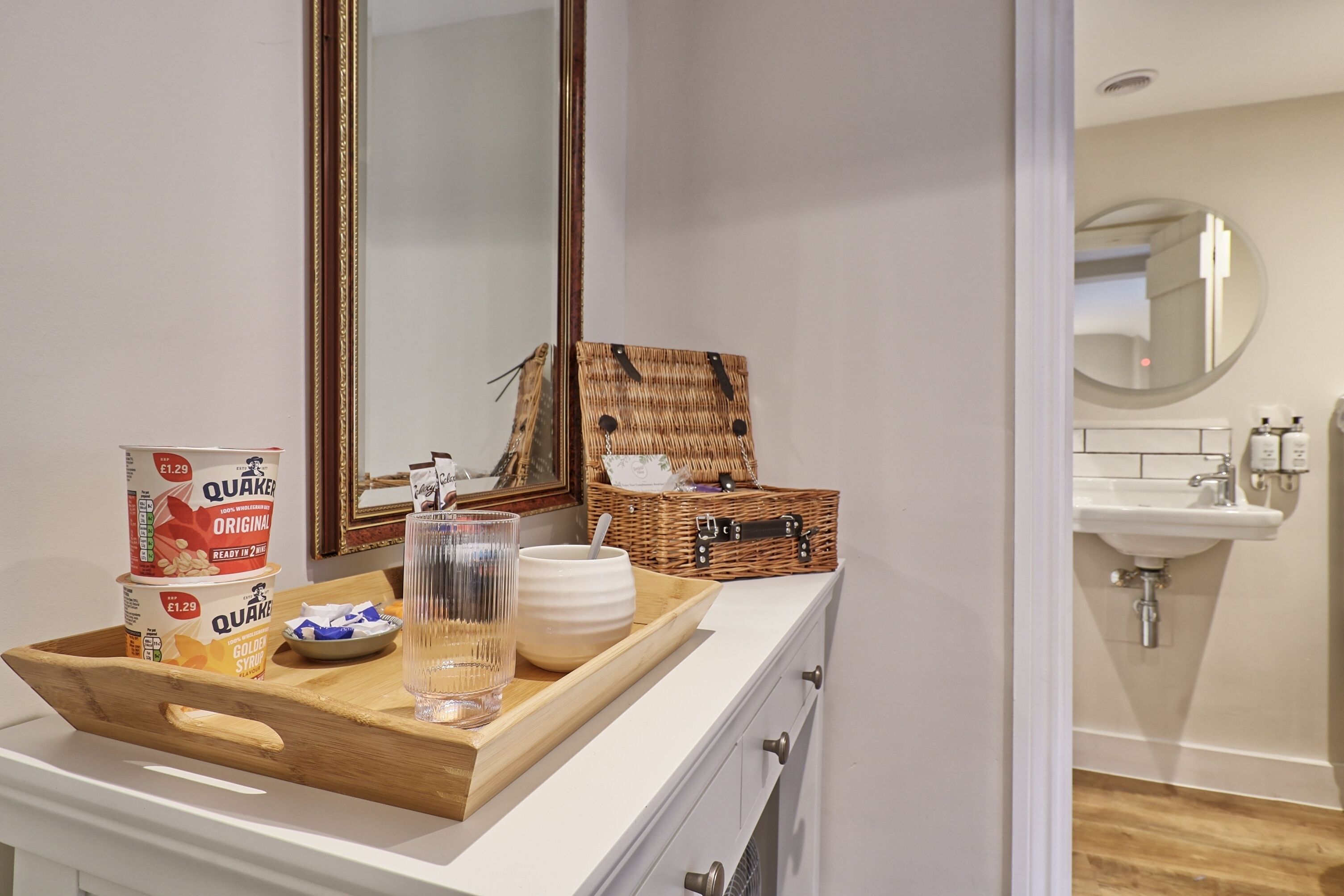 A bathroom with a sink, mirror, and a tray with Quaker Oats cereal boxes, a glass, and a basket.
