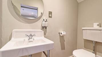 A bathroom with a white sink, a round mirror, a toilet, and a wall-mounted soap dispenser.