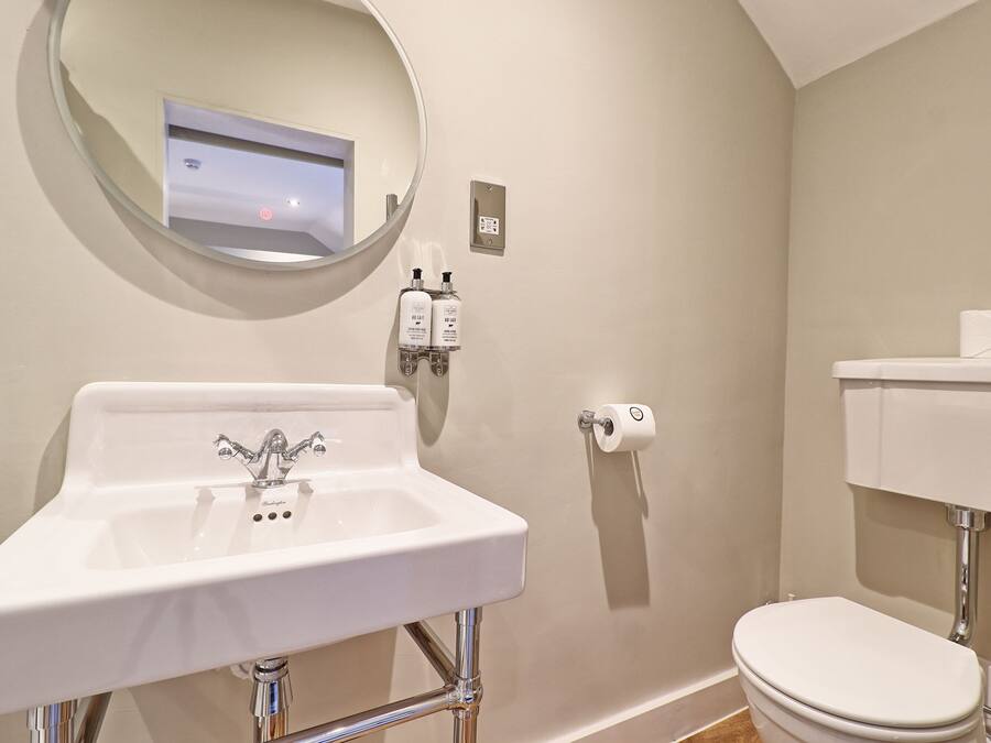 A bathroom with a white sink, a round mirror, a toilet, and a wall-mounted soap dispenser.
