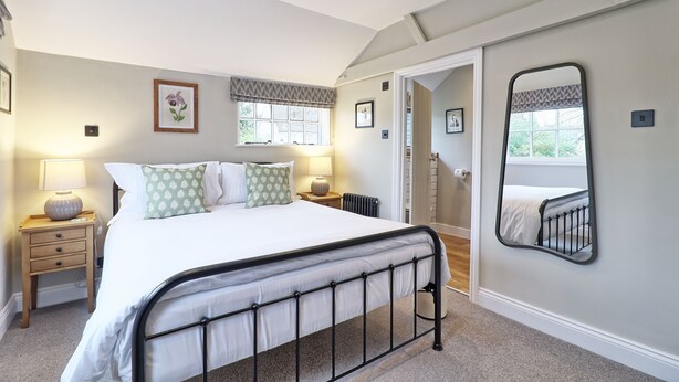 A bedroom with a bed, bedside tables, a mirror, and a window. - Noble Goose Rooms (Colchester)