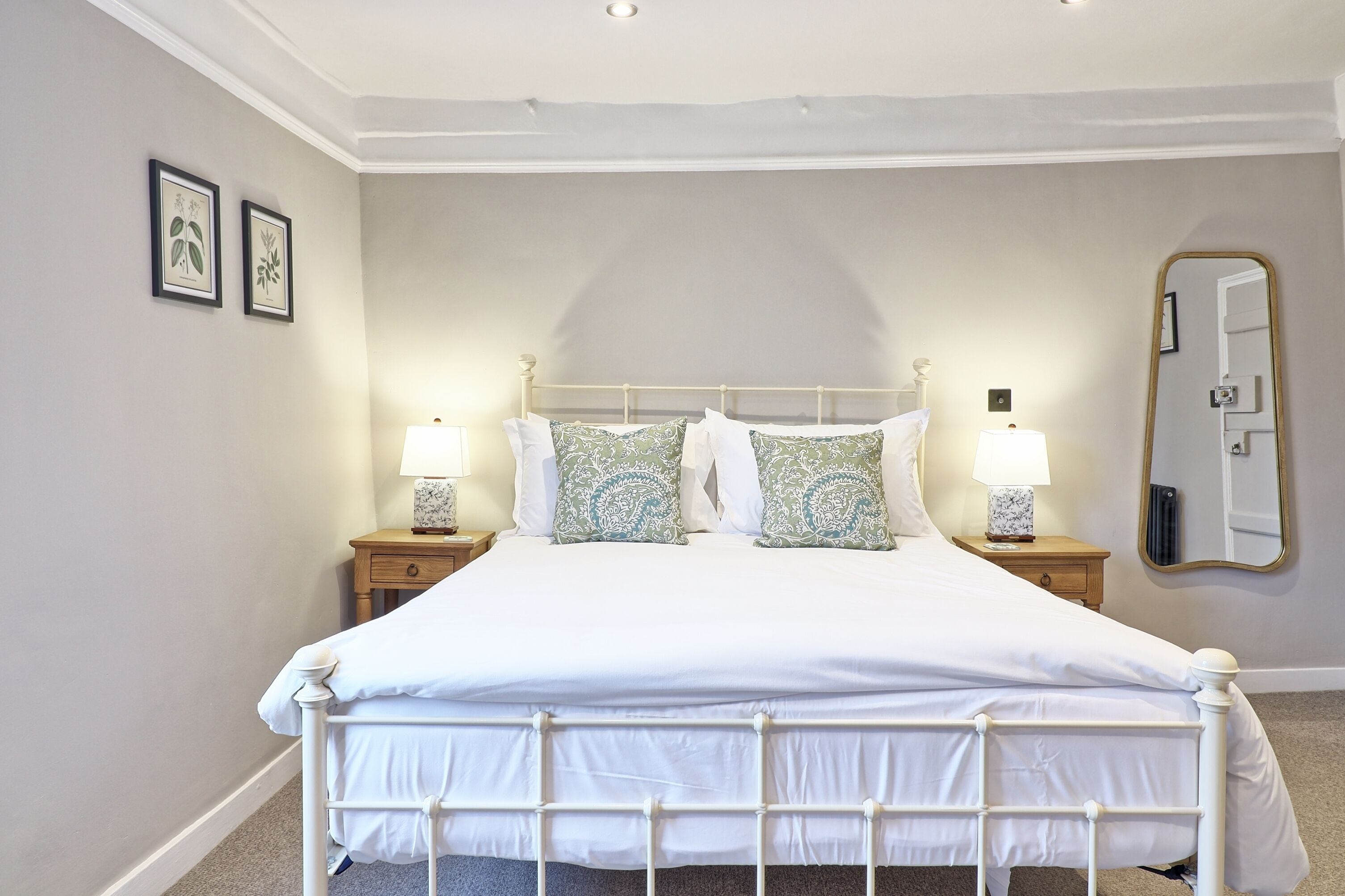 A neatly made bed with white bedding, two bedside tables with lamps, and a large mirror on the wall.