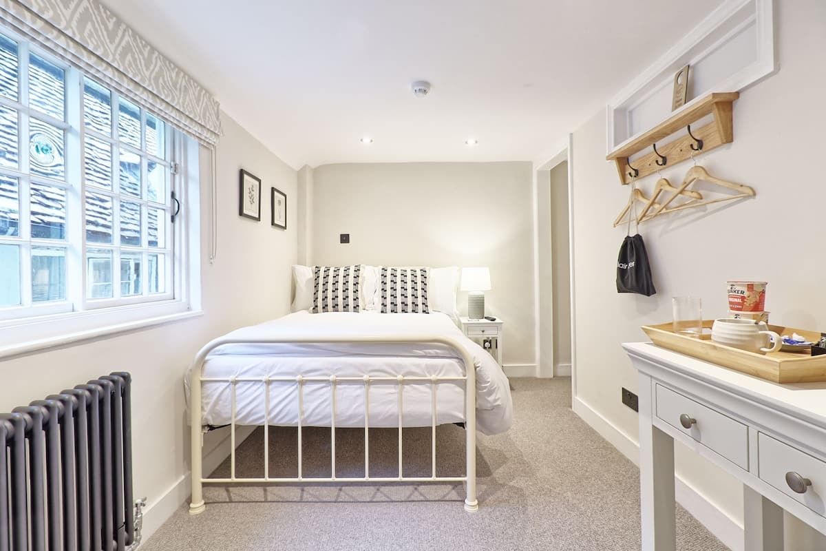 A bedroom with a bed, bedside table, lamp, radiator, and a dresser with a tray.