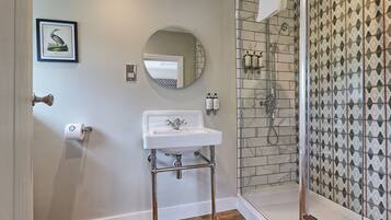 A bathroom with a white sink, a round mirror, a shower with a glass door, and patterned tiles on the walls.