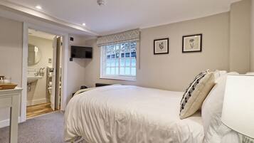 A bedroom with a bed, a window with curtains, a TV mounted on the wall, and a bathroom visible through an open door.
