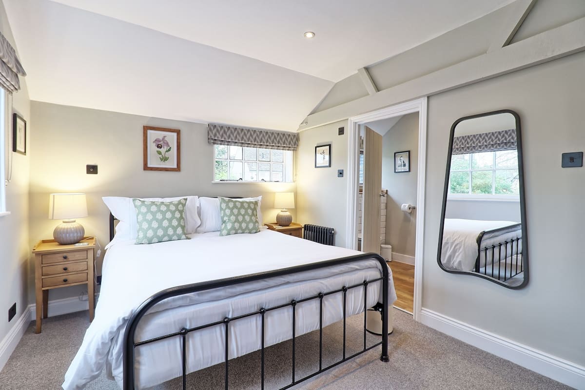 A bedroom with a bed, bedside lamps, a mirror, and a view of a staircase.