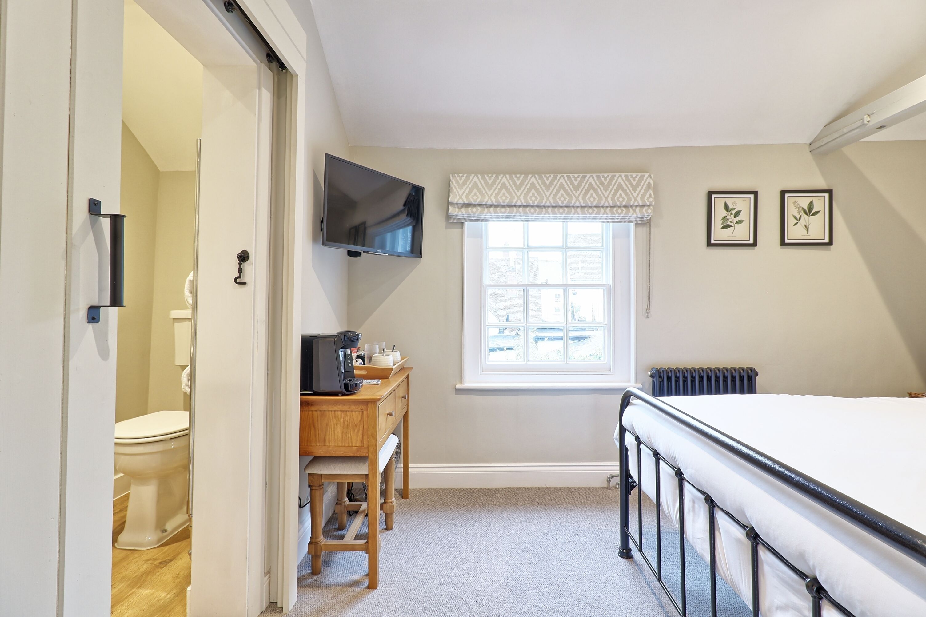 A bedroom with a bed, a desk with a chair, a television, a window with curtains, and a radiator.