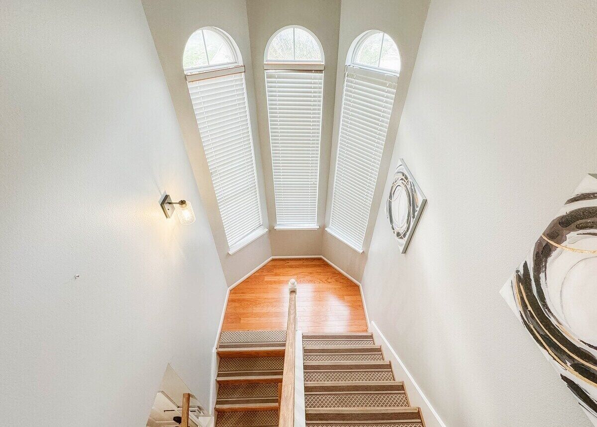 Una escalera de madera con barandilla que lleva a un rellano con tres ventanas de arco.