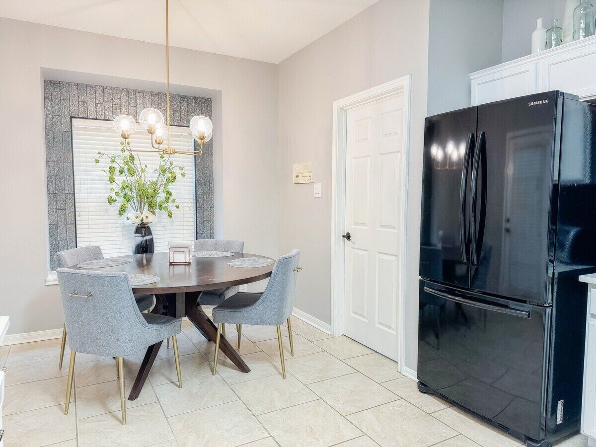 Una cocina moderna con un refrigerador negro, una mesa de comedor con cuatro sillas y una lámpara colgante.