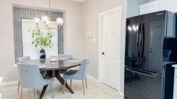 Una cocina moderna con un refrigerador negro, una mesa de comedor con cuatro sillas y una lámpara colgante.