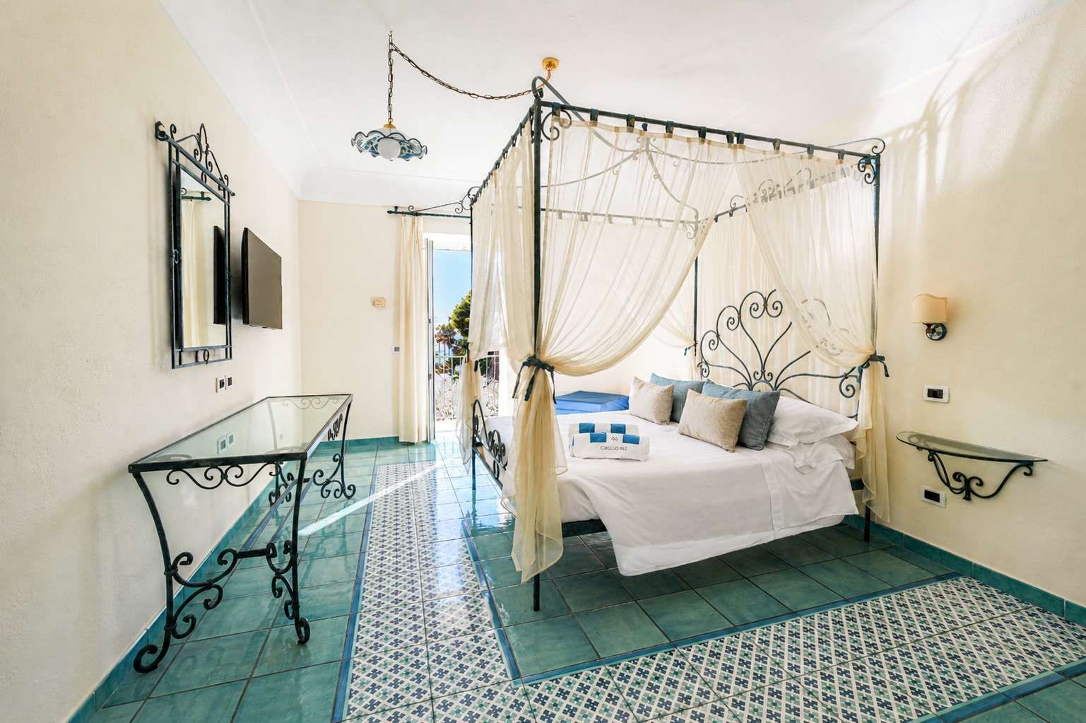 Quarto com cama de dossel, mesa de vidro e piso estampado.