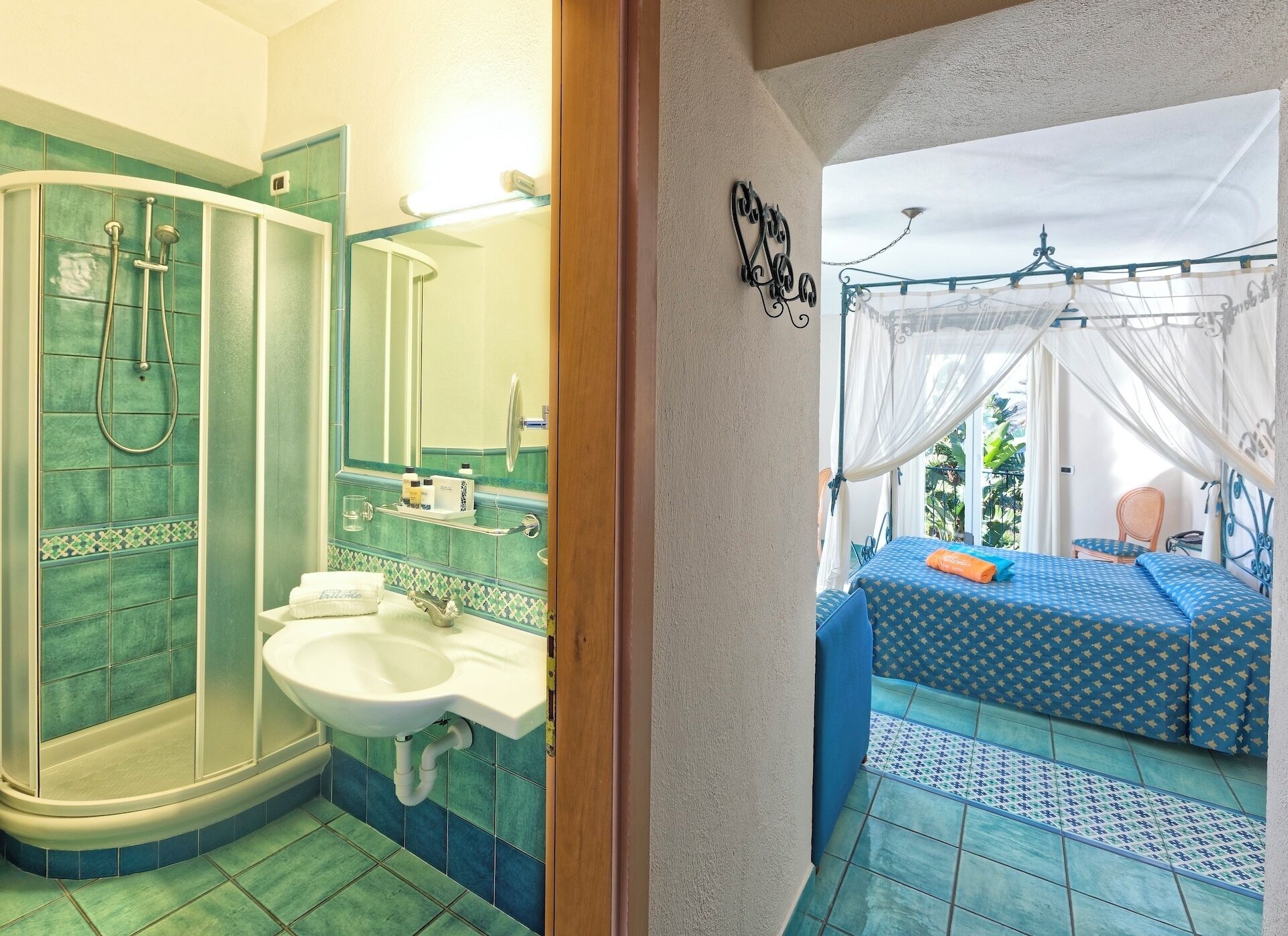 A bathroom with a shower, sink, and mirror. There is a bed with a canopy and a view of the outdoors.