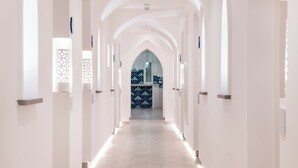 Un pasillo largo y estrecho con paredes blancas y suelo de baldosas, que conduce a una habitación con pared de diseño azul y blanco.