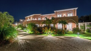 Un edificio de dos plantas con fachada simétrica, ventanas arqueadas y un camino de grava que conduce a la entrada.