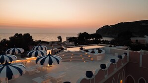 Una terraza en la azotea con mobiliario exterior, piscina y vistas al mar al atardecer.