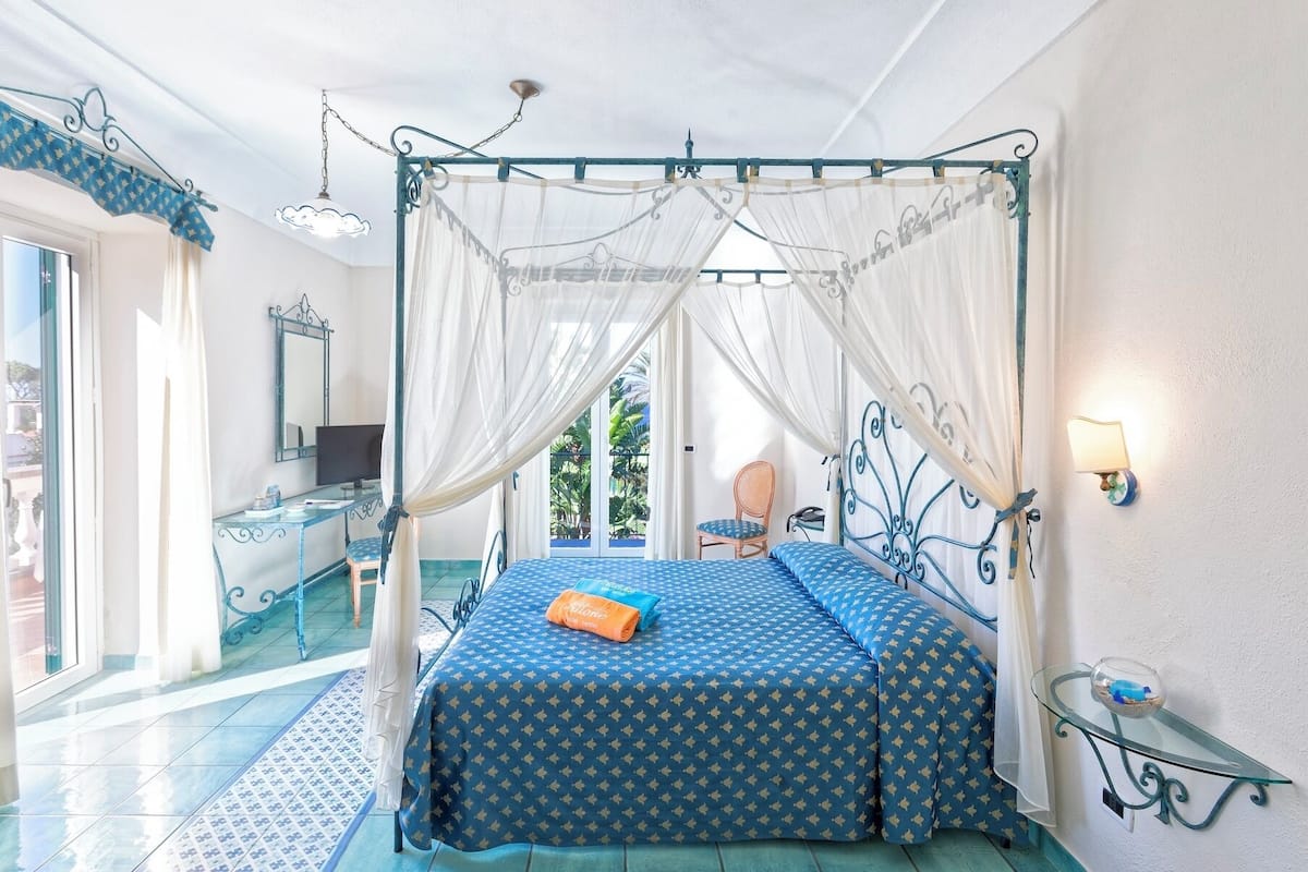 Una habitación con una cama con dosel, una mesita con lámpara y una silla.