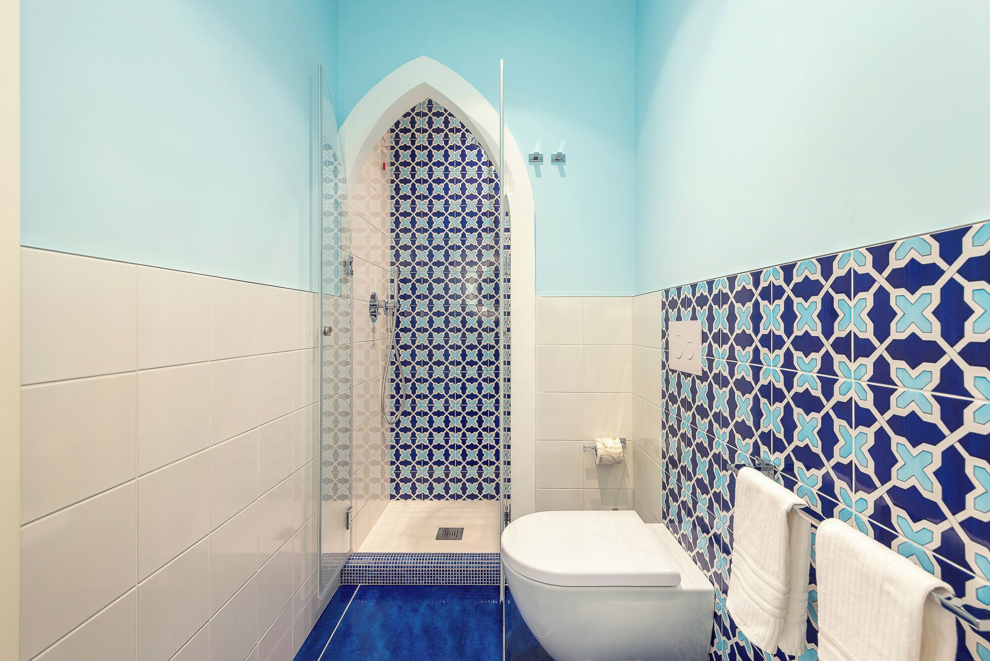 A bathroom with a shower, toilet, and patterned tiles.