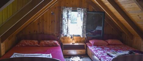 Une chambre mansardée chaleureuse avec deux lits, une fenêtre avec des rideaux et une petite table avec une lampe.