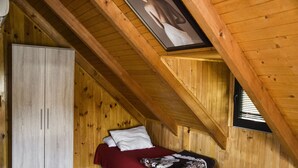 A bedroom with a sloped ceiling, wooden walls, a bed with red bedding, and a wardrobe. - Genti House Ada Bojana (Ulcinj)