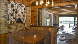 A wooden interior with a brick wall, a dining area with a table and chairs, and a view into a kitchen area. - Genti House Ada Bojana (Ulcinj)
