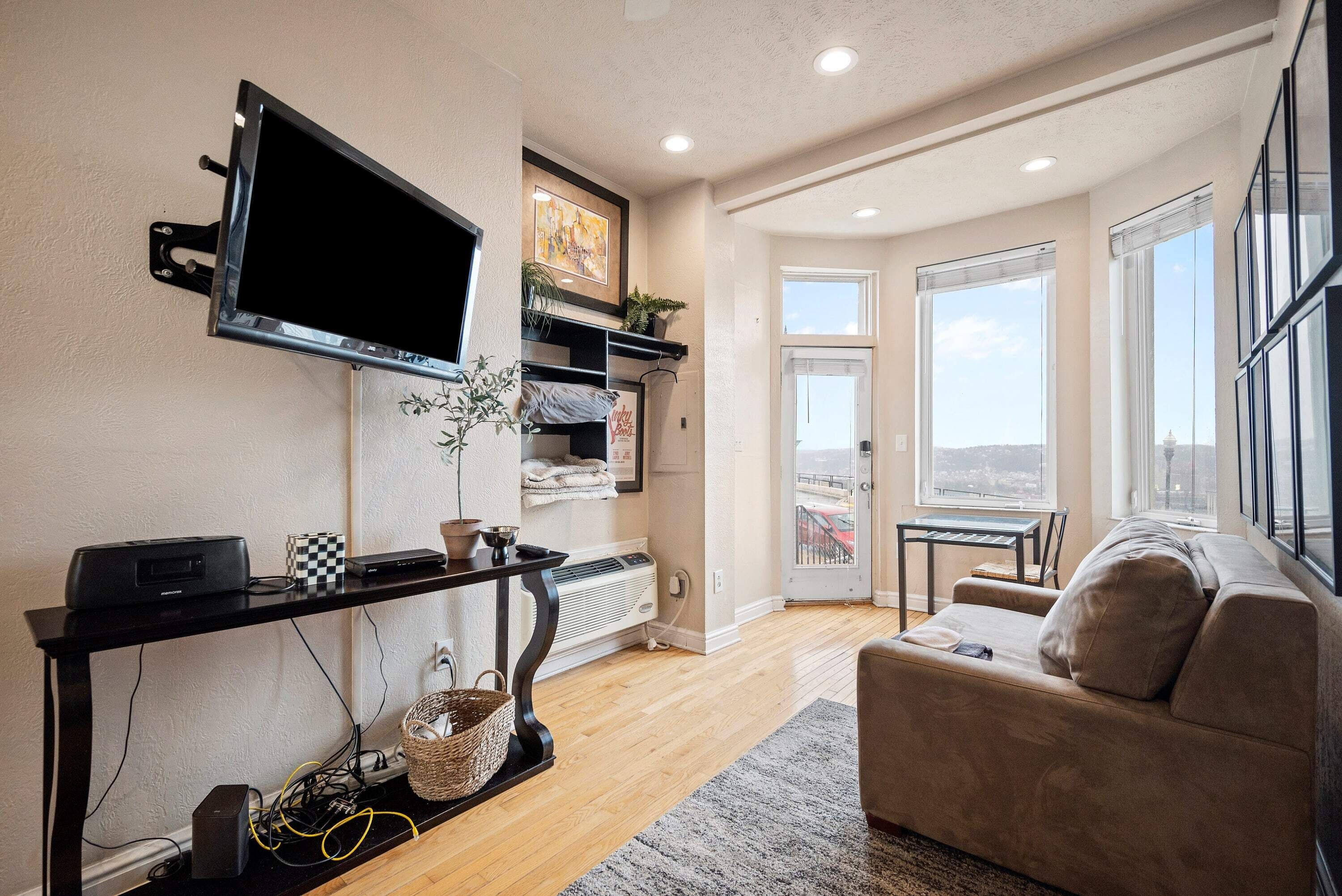 A modern living room with a flat-screen TV, a sofa, a coffee table, and a view of the city through large windows.